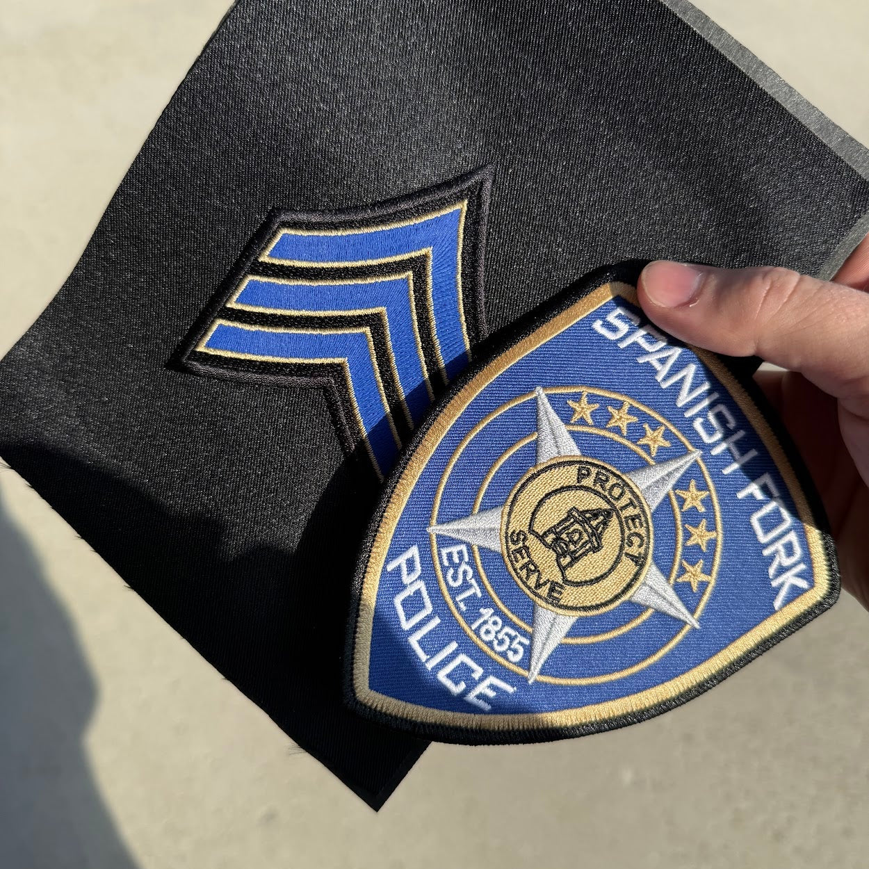 Hand holding a Spanish Fork Police patch on a black surface