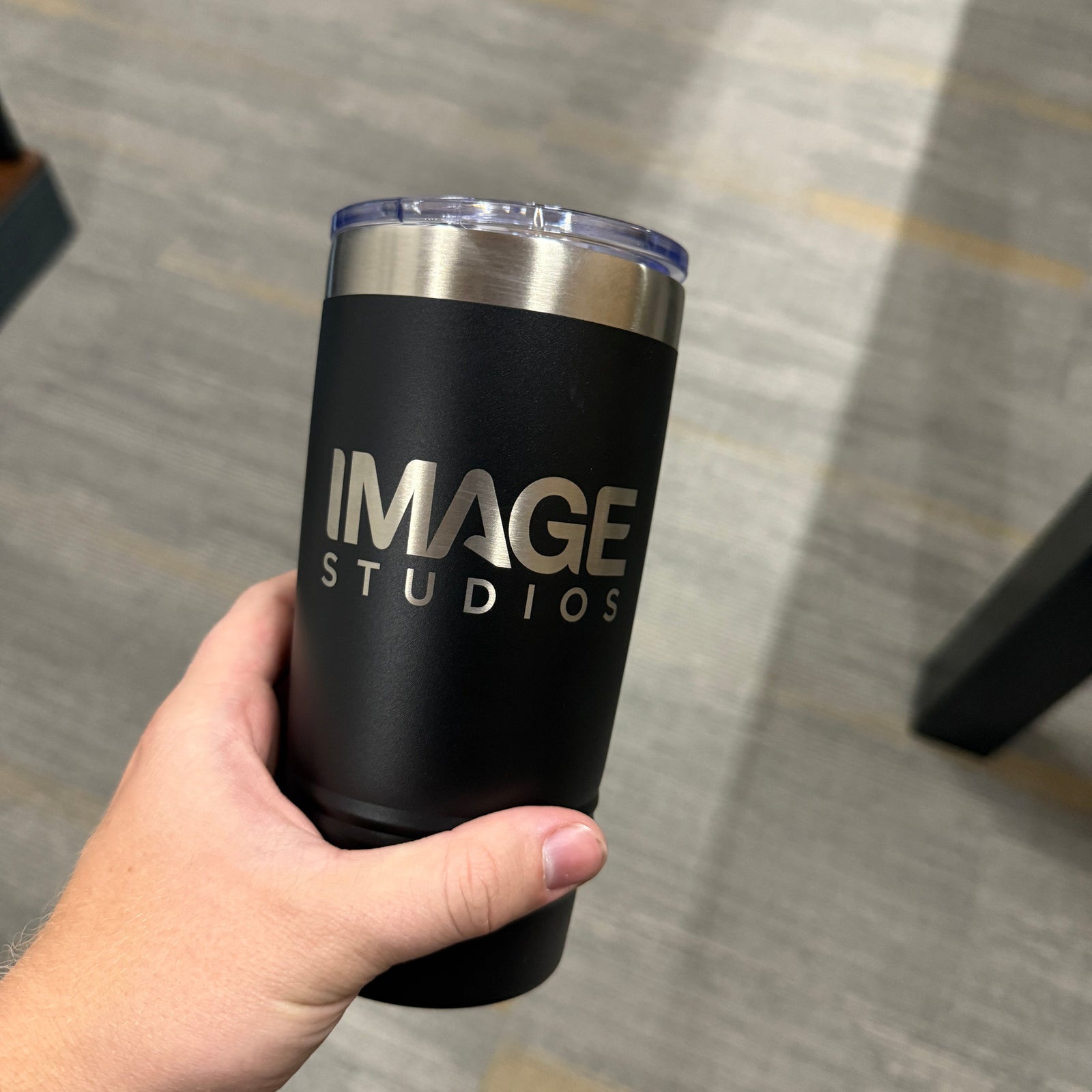 Black tumbler with 'IMAGE STUDIOS' branding held by a hand on a gray floor.
